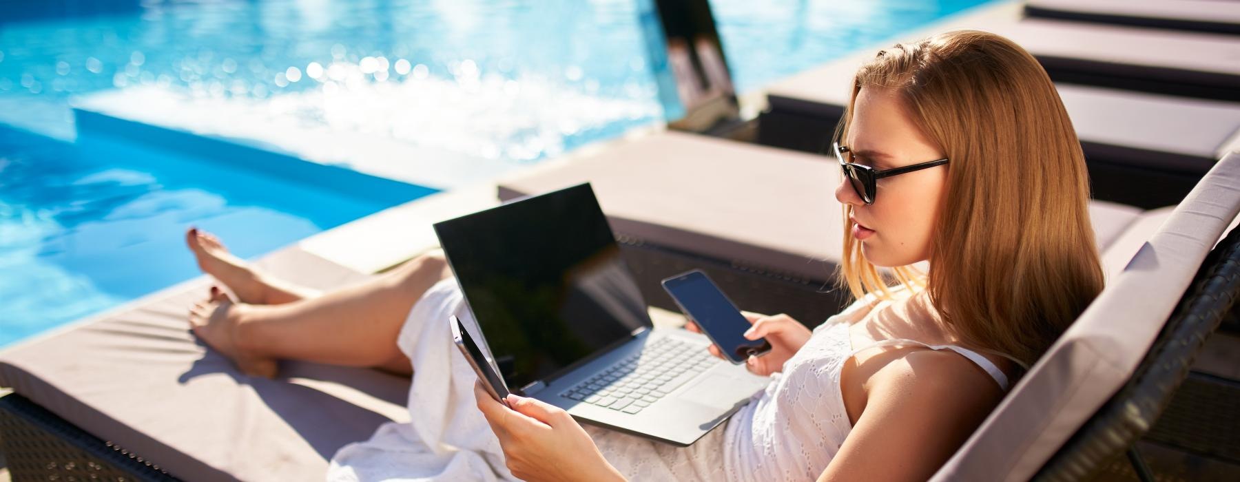 a woman sitting in a chair with a laptop by a pool