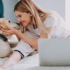 a woman with a laptop and a dog on a bed